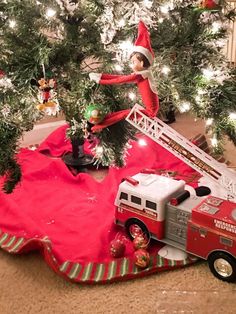 an elf is on top of a ladder next to a christmas tree and firetruck