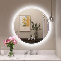 a bathroom sink with a round mirror above it and flowers in a vase on the counter