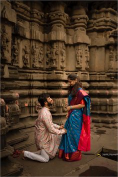 a man kneeling down next to a woman in front of a stone structure with carvings on it