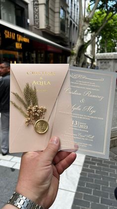 a person holding up a wedding card with a gold seal on the front and side