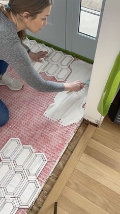 a woman in grey shirt and jeans laying on floor next to wall with white tile