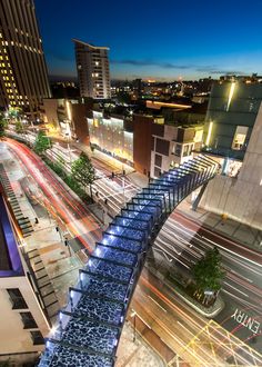 an aerial view of a city street at night with lights and buildings in the background