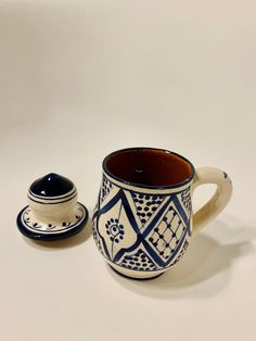 a blue and white coffee cup sitting next to a small ceramic container on a white surface