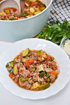 a white bowl filled with meat and vegetables next to a pot of soup on a table