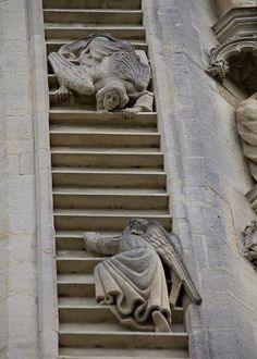 statues on the side of a building with stairs leading up to it and another statue in the background