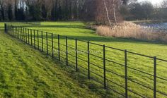 a long black fence in the middle of a grassy field next to a body of water