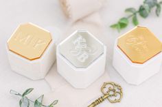 three white boxes with gold foil on them sitting next to a key and some greenery