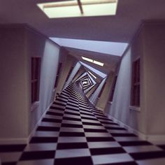 an empty hallway with black and white checkered flooring on both sides, leading up to the skylight