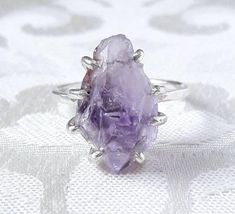 The beautiful rough amethyst crystal in this ring is completely gorgeous! Totally untreated and uncut, the natural facets and smooth crystal faces reflect light, while inside the crystal glitters with ridges and rainbow-like inclusions. The fascinating stone is set in a hand-made sterling silver claw setting and placed on a hammered sterling silver band. This lovely, slightly rustic ring would be a perfect gift for a February baby (or the mother of one!), or for someone special who deserves a tr Purple Crystal Ring, Raw Stone Engagement Rings, Amethyst Wedding Rings, Raw Amethyst Crystal, February Baby, February Birthstone Ring, Birthstone Ring Mothers, Funky Rings, Rustic Ring