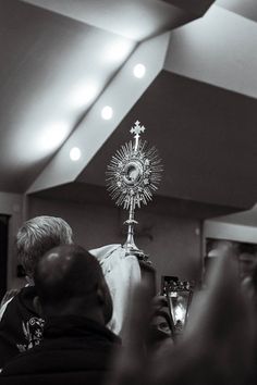 a black and white photo of a priest holding the cross in front of his head