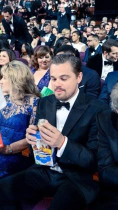 a man in a tuxedo is looking at his cell phone while people stand around him