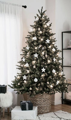 a christmas tree in a living room with white lights and presents on the floor next to it