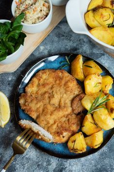 a plate with fish and potatoes on it next to bowls of vegetables, lemon wedges and bread