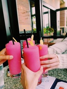 three people holding up pink drinks at a table