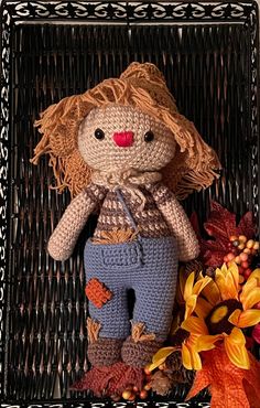 a crocheted doll sitting on top of a basket next to autumn leaves and flowers