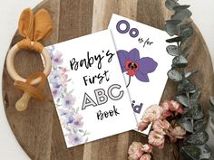 two baby's first abc book on a wooden table next to flowers and rubber rings