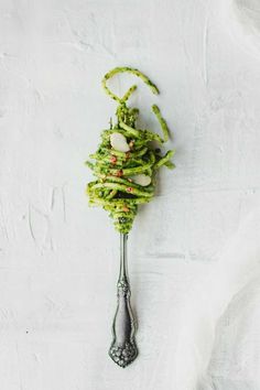 a spoon with some food on it sitting next to a white wall and table cloth