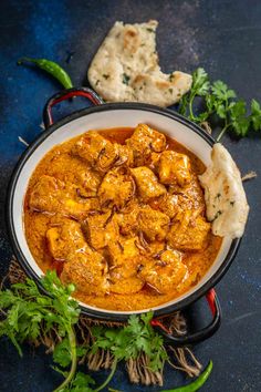 chicken curry in a white bowl with garnishes and bread on the side