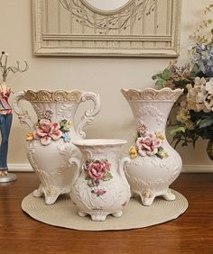 three white vases sitting on top of a wooden table next to flowers and a clock