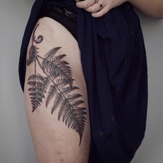 a woman with a tattoo on her thigh holding onto a black and white fern leaf