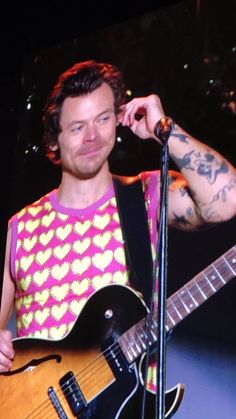 a man with tattoos on his arm holding a guitar in front of a microphone and looking at the camera