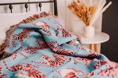 a bed with a blue and pink blanket on top of it next to a white table