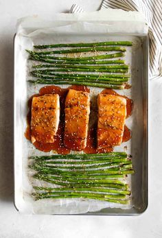 salmon and asparagus on a baking sheet with brown sauce in the middle, ready to be cooked