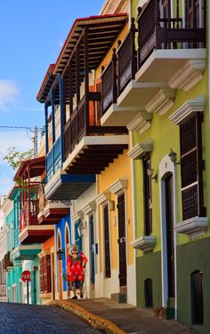 a woman walking down an empty street in front of colorful buildings with balconies