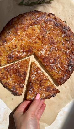 a person holding a piece of pizza in front of a pie on top of a table