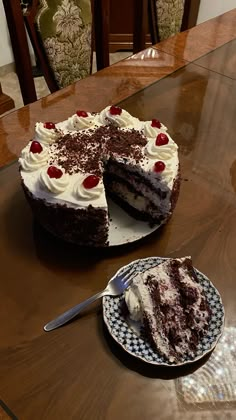 a chocolate cake with white frosting and cherries on top sitting on a table