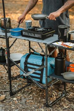 a man cooking food on top of a table with a grill in the back ground