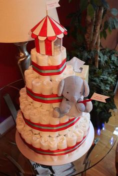 a diaper cake with an elephant on top and baby items around the bottom, sitting on a glass table