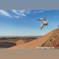 a man flying through the air while riding a skateboard on top of a sand dune