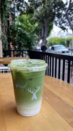 a green drink sitting on top of a wooden table next to a tree in the background