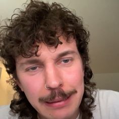 a close up of a person with curly hair and a moustache on his face