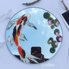 there is a mirror with a fish in it on the table next to some flowers