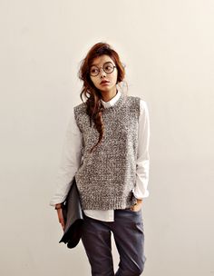 a young woman wearing glasses and a sweater is standing in front of a white wall