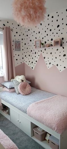 a pink and black bedroom with polka dots on the wall, white bedding and drawers