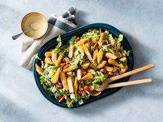 a salad with chicken, lettuce and tomatoes in a blue bowl next to two wooden spoons