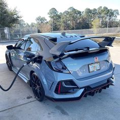 an electric car plugged in to a charging station with its hood open and it's tail lights on