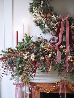 a fireplace mantel decorated with christmas wreaths and pink ribbon tied around the mantle