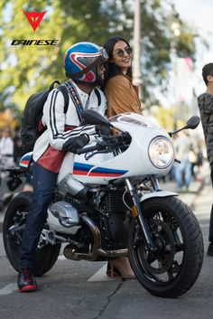 a man and woman sitting on a white motorcycle in the street with other people standing around