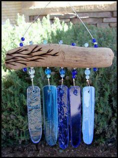 four different colored glass pieces hanging from a tree branch in front of some shrubbery