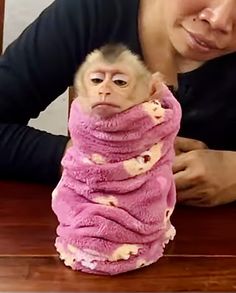 a woman holding a stuffed monkey wrapped in pink material on top of a wooden table