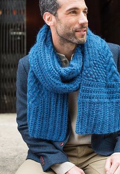 a man sitting on the ground wearing a blue knitted scarf and sweater over his shoulders