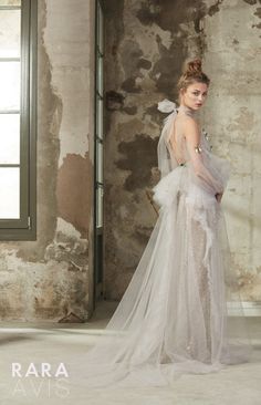 a woman in a white wedding dress standing next to an old brick wall and window