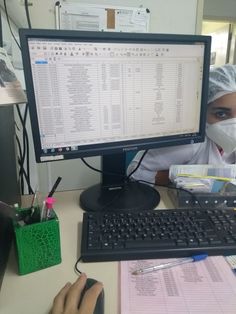 a person wearing a surgical mask sitting at a desk in front of a computer monitor