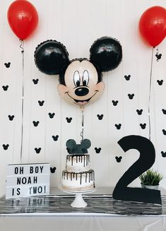 a mickey mouse cake and balloons on a table with a number two sign in front of it