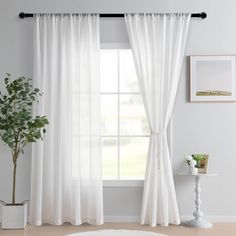 a living room with white curtains and a potted plant