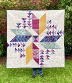 a person standing in the grass holding up a quilt